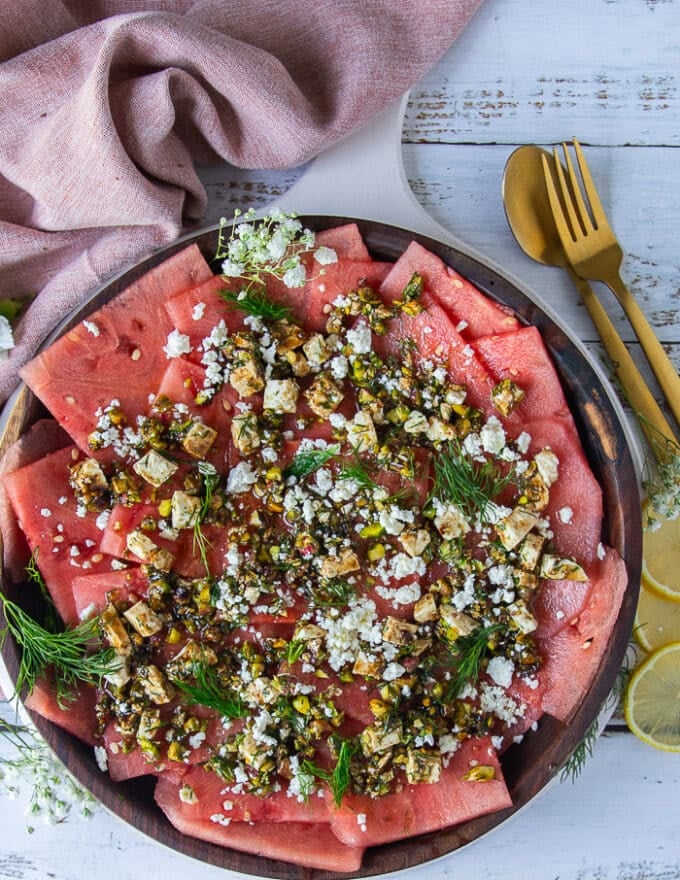 A plate of carpaccio recipe made with watermelon topped with feta, pistachio , dill, lemon and olive oil