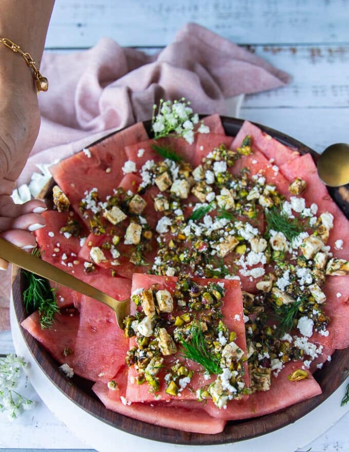 A hand holding a spoon with watermelon carpaccio showing how to serve it