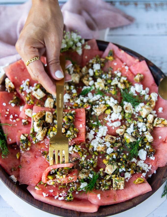 A spoon taking a chunk serving of watermelon carpaccio with the topping and everything showing close up details