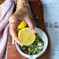 The carpaccio ingredients are placed in a bowl along with olive oil, balsamic and a hand holding half a lemon squeezing the lemon juice in