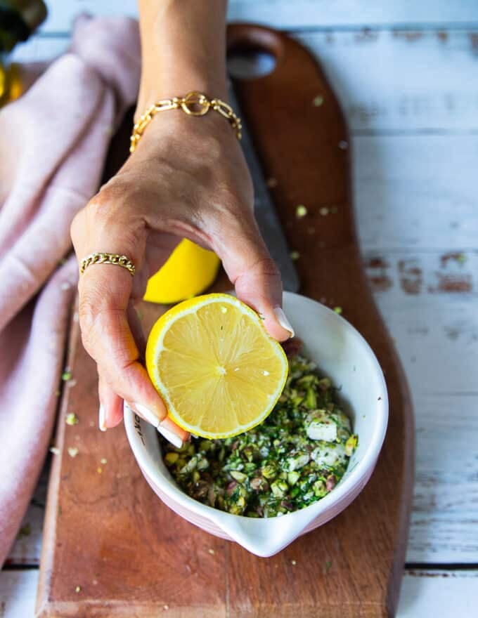 The carpaccio ingredients are placed in a bowl along with olive oil, balsamic and a hand holding half a lemon squeezing the lemon juice in