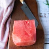 A block of watermelon on a wooden board and a sharp knife around it