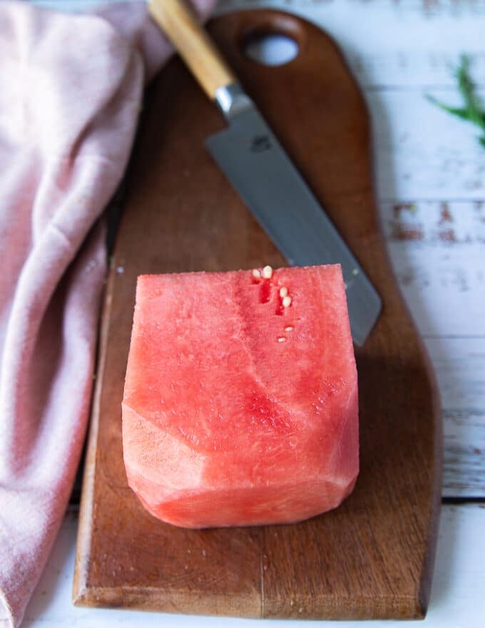 A block of watermelon on a wooden board and a sharp knife around it