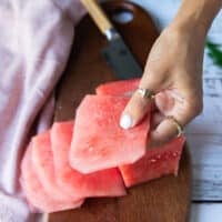 A hand holding a thinly sliced watermelon showing how to make carpaccio slices