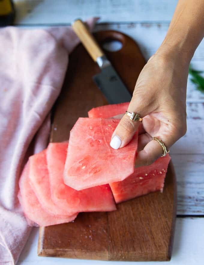 A hand holding a thinly sliced watermelon showing how to make carpaccio slices