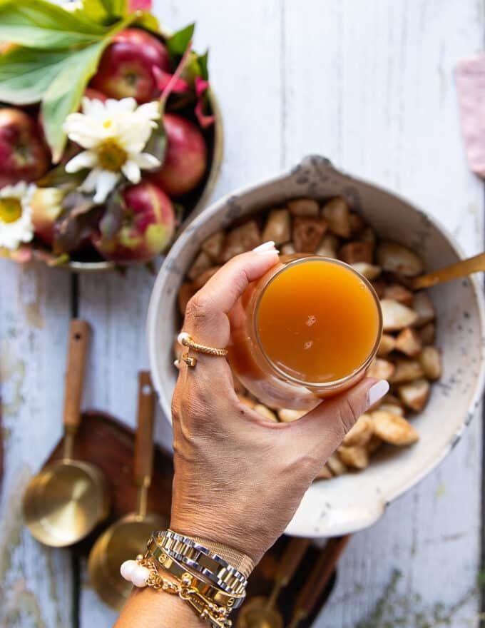 A hand holding apple cider adding it to the apples for the instant pot