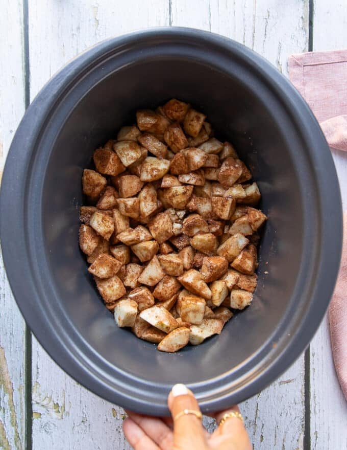 The apple mixture added to the bowl of a crockpot and set to slow cook.