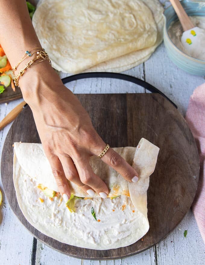 second step to fold a wrap is a hand showing how to fold the sides over the center to encompass the filling inside