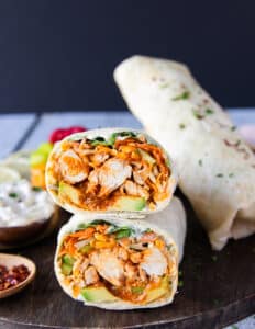close up of a cut up buffalo chicken wrap showing the inside layers of buffalo chicken, veggies cheese, sauce wrapped in tortilla