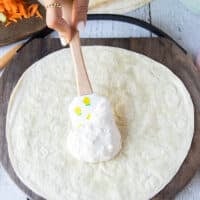 A spoon spreading some blue cheese dressing at the base of a flour tortilla