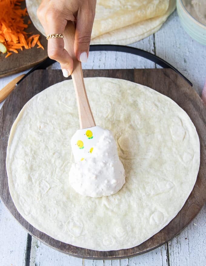 A spoon spreading some blue cheese dressing at the base of a flour tortilla