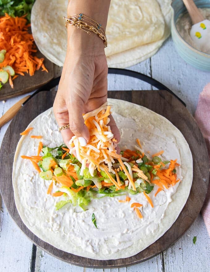 A hand adding the shredded cheese and carrots as part of the toppings