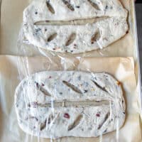 The two fougasse breads on a baking sheet covered with plastic wrap and ready for the second rise before baking