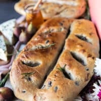 One Fougasse bread on a white board close up showing the add ins and the golden bread shaped like a leaf