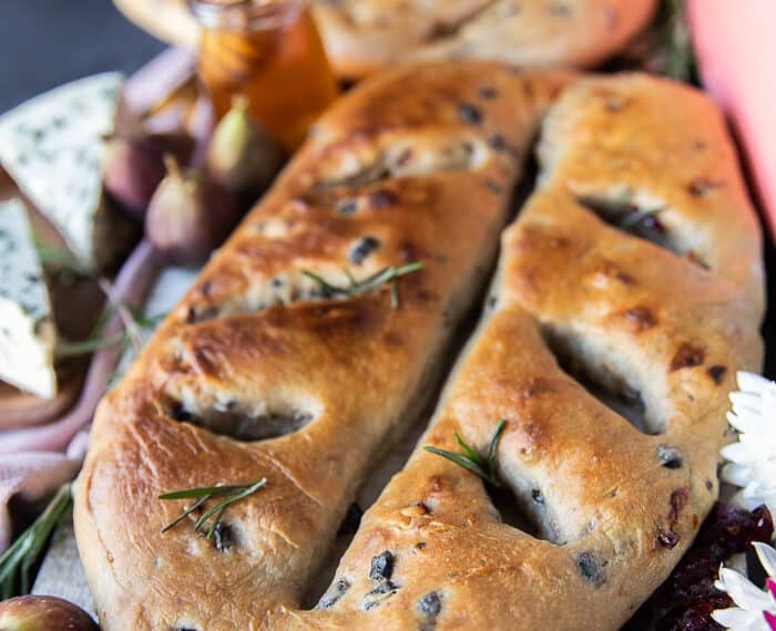 One Fougasse bread on a white board close up showing the add ins and the golden bread shaped like a leaf