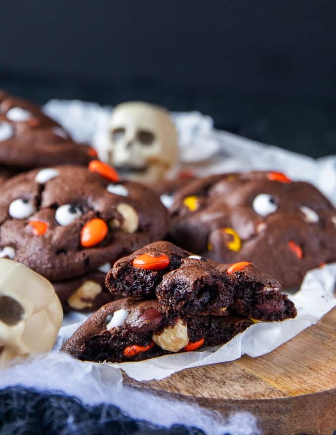 One broken up halloween cookie over a plate of other cookies and surrounded by skulls