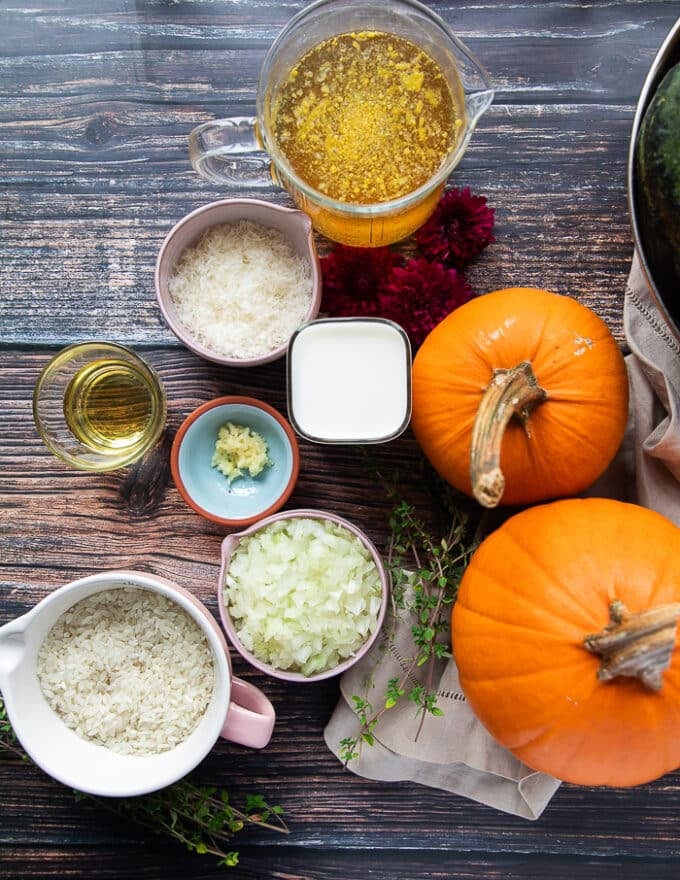 ingredients for pumpkin risotto including fresh pumpkins, a bowl of diced onions, some garlic, a bowl of stock, some milk, a knob of butter, a bowl of arborio rice , seasoning, some freshly grated parmesan cheese