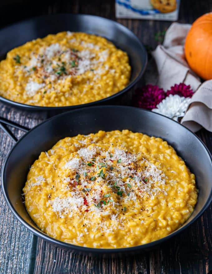 two plates of pumpkin risotto served and garnished on a wooden table