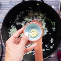 A hand holding a bowl of minced onions ready to add in the pot of risotto