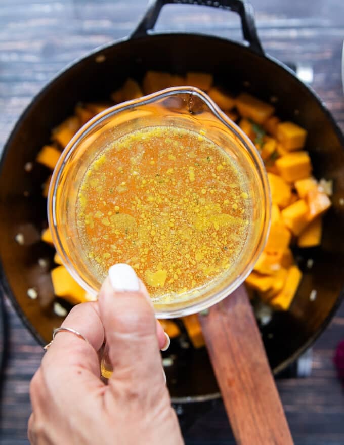 A hand holding stock and ready to pour it into the pot of pumpkin