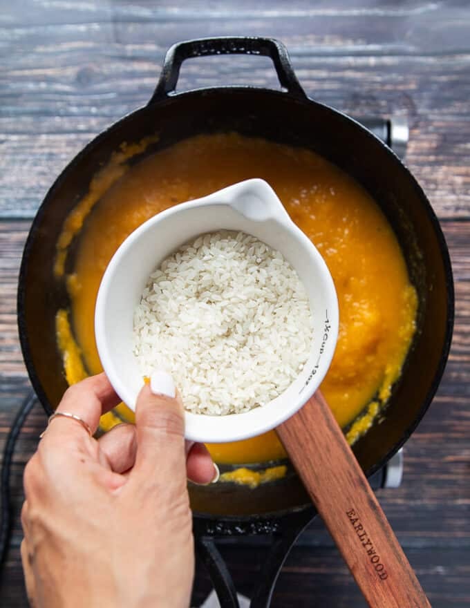 A hand holding a cup of arborio rice and ready to pour it into the pot to make risotto
