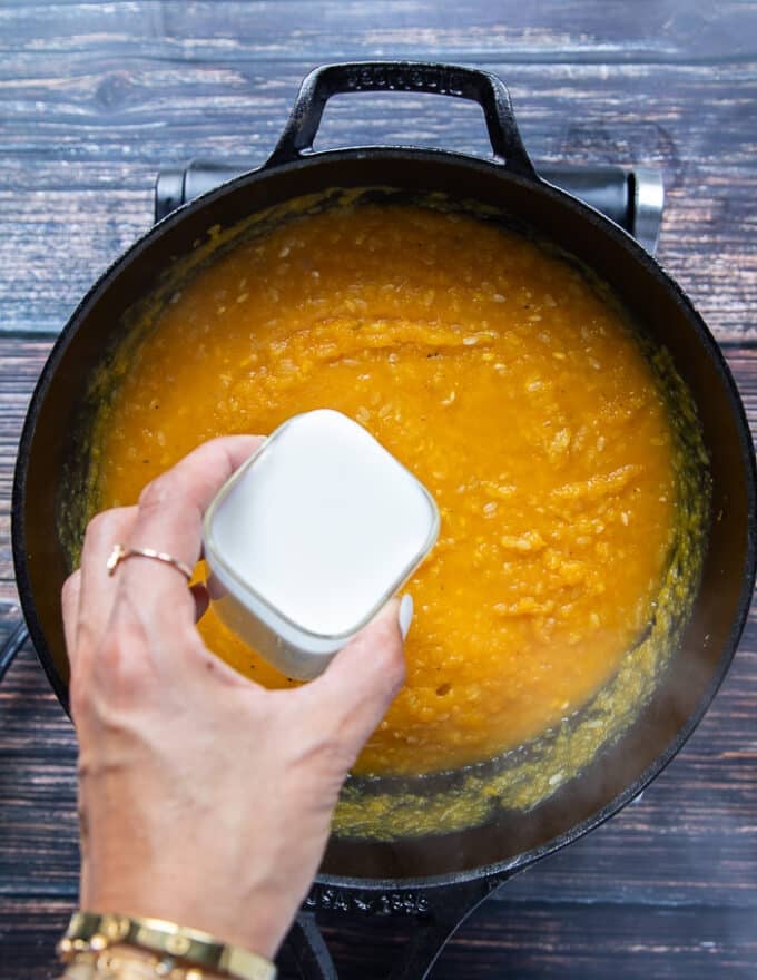 A hand adding in milk to the risotto pot for a creamier risotto