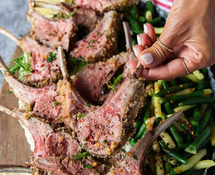 A hand holding a piece of lamb chop cut off from the rack of lamb to show the doneness