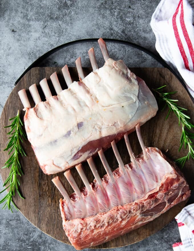 two french cut pieces of rack of lamb raw on a wooden board showing one flip side with the fat and the other with the bone