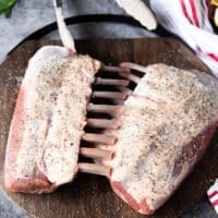 Two French cut racks of lamb on a wooden board seasoned with salt and pepper liberally on both sides