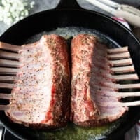 two french cut racks of lamb searing in a pan with melted butter