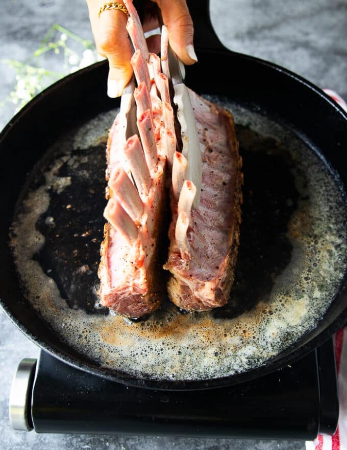 The rack of lamb is held straight to get all sides of it seared 