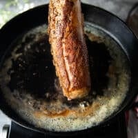 Final seared rack of lambs with a golden crisp buttery crust shown close up and placed on a rack