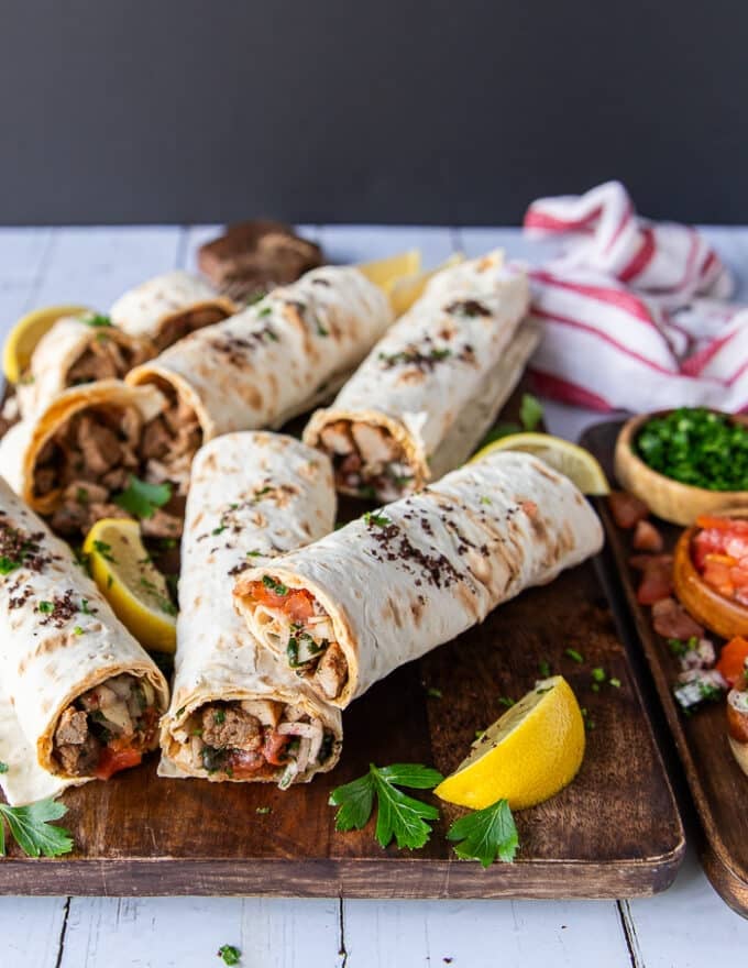 A wooden board with 4 tantuni sandwiches cut up and served with lemon wedges, extra parsley on the side and sumac bowl.