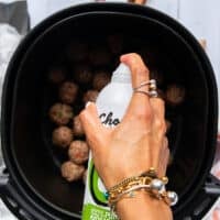A hand spraying some oil spray over the meatballs in the air fryer