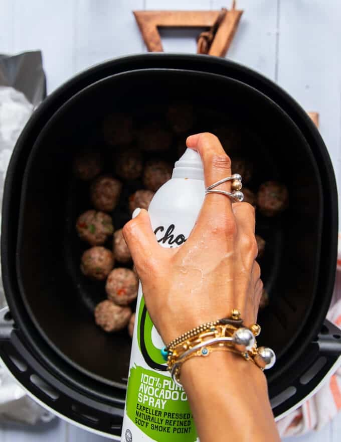 A hand spraying some oil spray over the meatballs in the air fryer