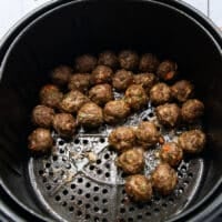 Shaking the air fryer halfway showing the progress of air frying the meatballs