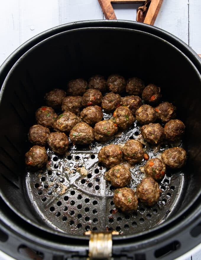 Shaking the air fryer halfway showing the progress of air frying the meatballs