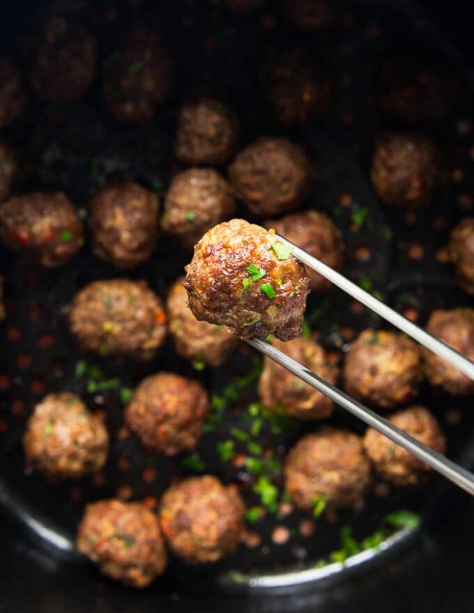 The air fryer meatballs ready and cooked, and a tong holding one meatballs close enough to show the details of the cooked air fryer meatballs