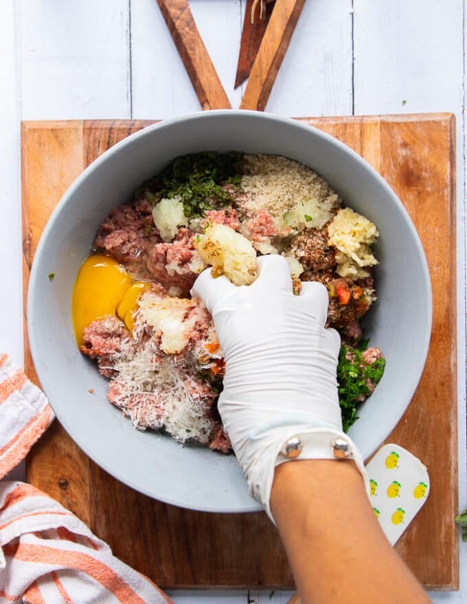 A hand wearing a plastic glove mixing the meat and ingredients together