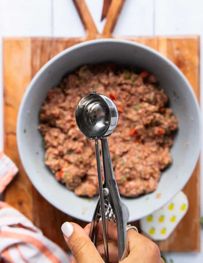 A hand holding an ice cream scoop to start portioning the matballs recipe