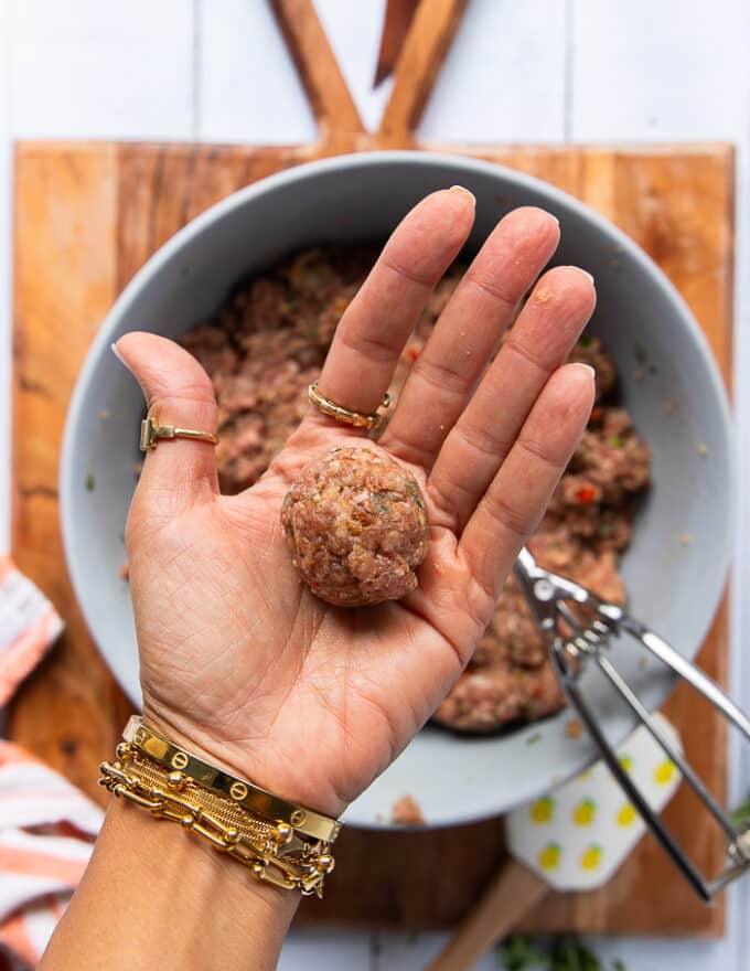 A hand holding the scoop of meat mixture and rolling it into a perfect shape