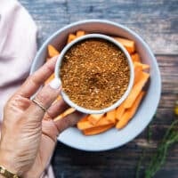 A hand holding a dry spice blend in a plate with a teaspoon of chilli powder, garlic powder, salt, pepper, oregano