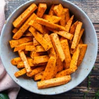 Sweet potato fries in a large bowl tossed with olive oil and a seasoning blend before it goes into the air fryer.