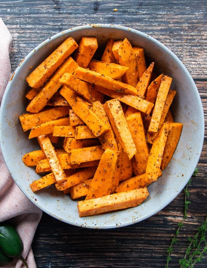 Sweet potato fries in a large bowl tossed with olive oil and a seasoning blend before it goes into the air fryer. 