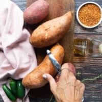 A hand peeling off the sweet potatoes using a vegetable peeler