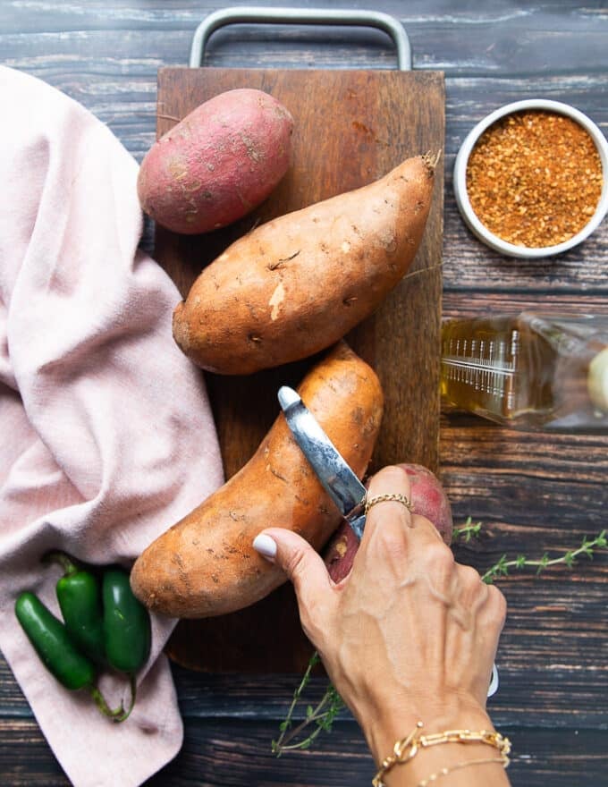 A hand peeling off the sweet potatoes using a vegetable peeler