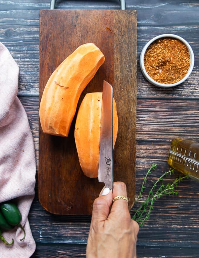 A hand cutting the sweet potatoes into half