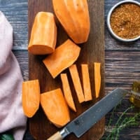 A hand cutting half an inch strips of the sweet potatoes to look like fries