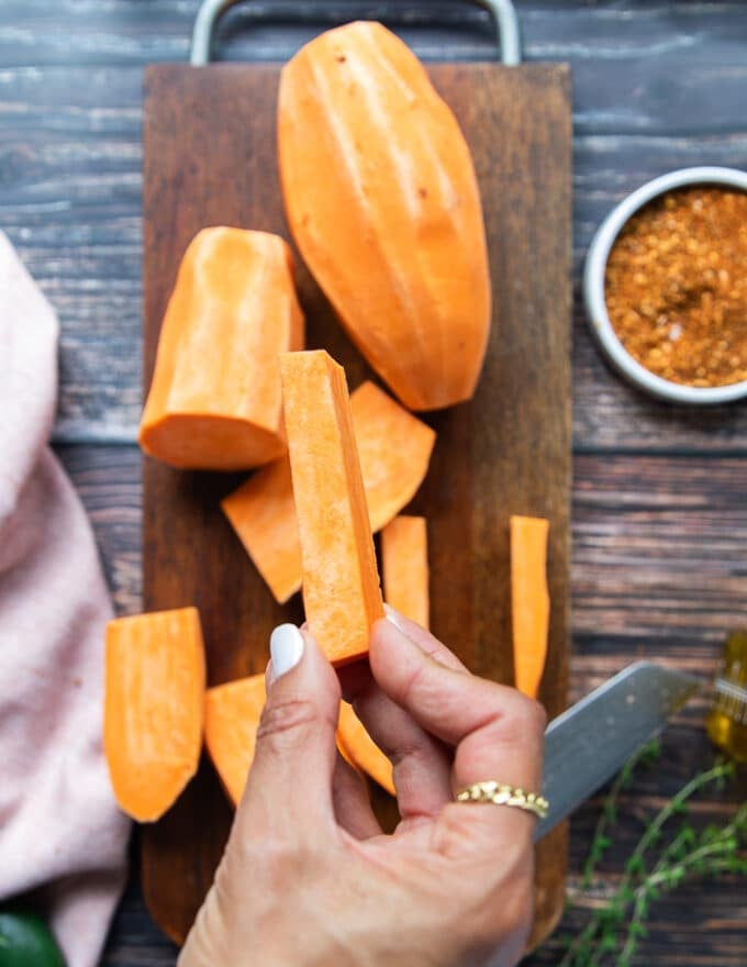 A hand holding a piece of cut up sweet potato fries showing the size of it. 