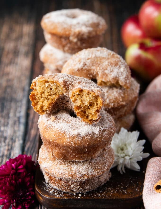 an apple cider donut cut in half placed over the stacks of donuts to show how the texture looks